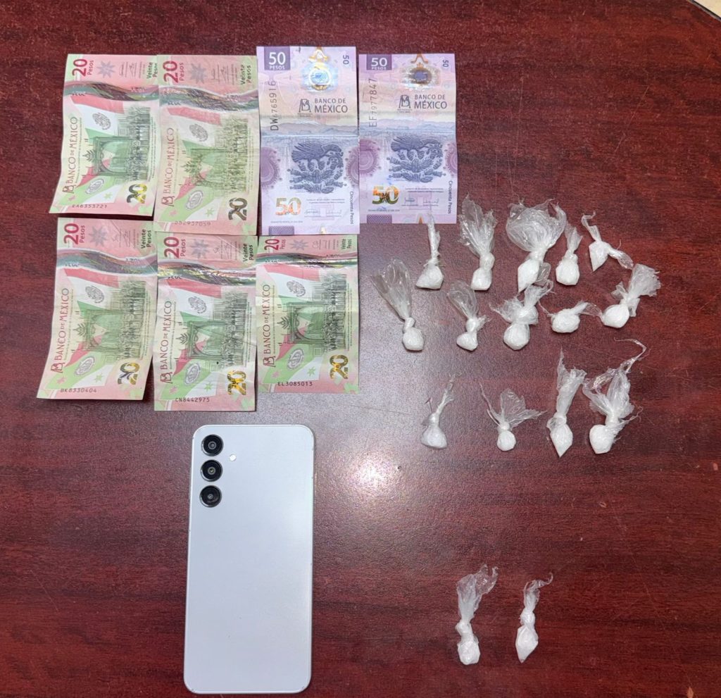 drogas encontradas - PUNTO DE ENCUENTRO Stacks of Mexican 20- and 50-peso bills laid out on a wooden table next to several small plastic bags containing a white powder and a white smartphone nearby.