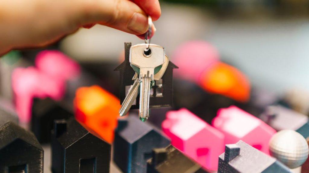 quantium-desarrollos-pedro-dávila-depa-casa-monterrey - PUNTO DE ENCUENTRO Hand holding a keyring with keys above a row of miniature houses, symbolizing home ownership or real estate.
