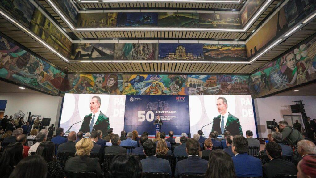 Speaker at a podium on a stage during a formal 50th anniversary municipal event, with large screens and an attentive audience.